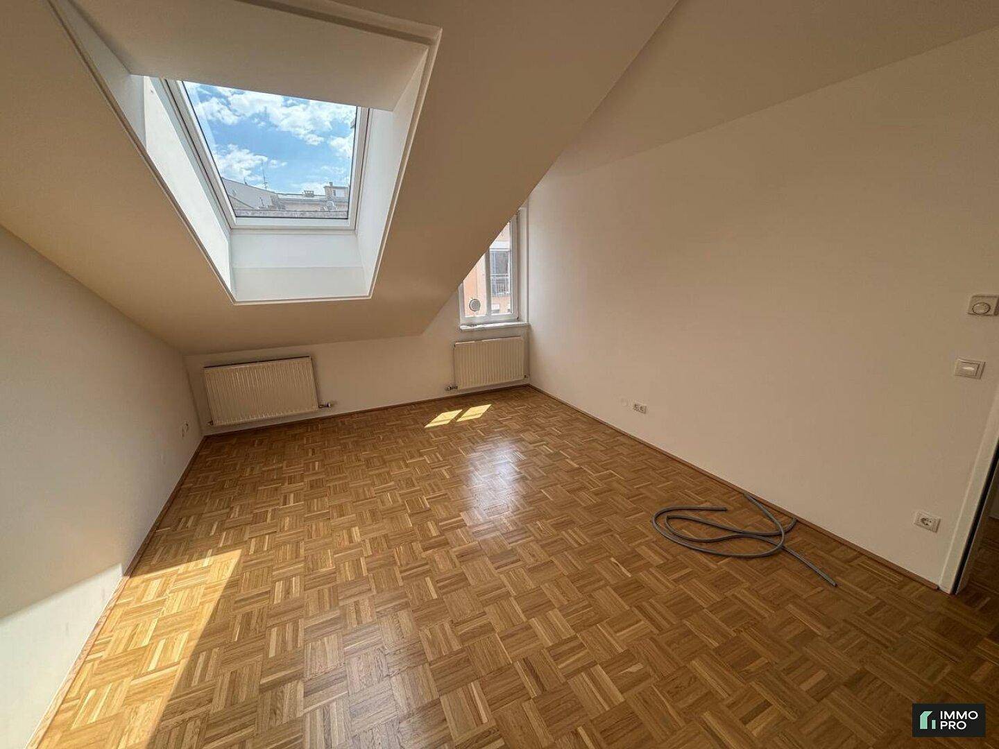 Lichtdurchflutetes Dachgeschosszimmer mit Parkettboden, großem Dachfenster und Ausblick.