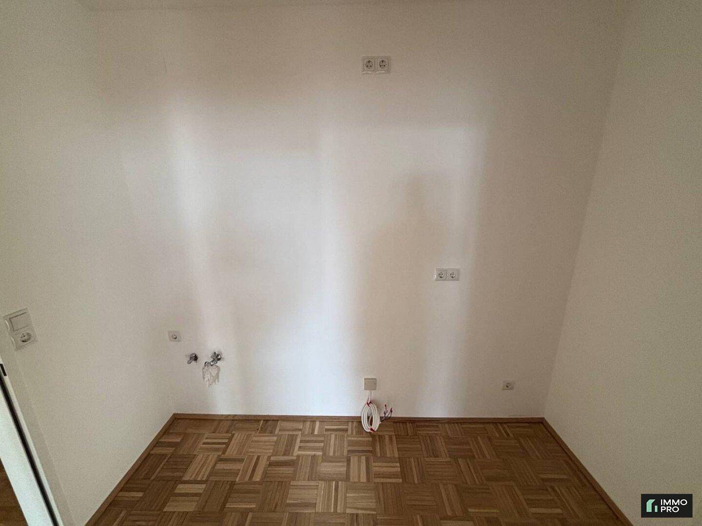 Leerer Küchenraum mit Parkettboden, Anschlüssen für Geräte und Steckdosen.