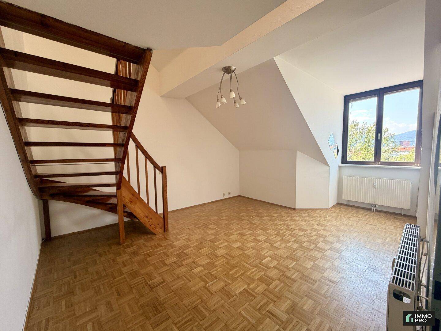 Heller Wohnbereich mit Holztreppe, Parkettboden und Fenster mit Ausblick.