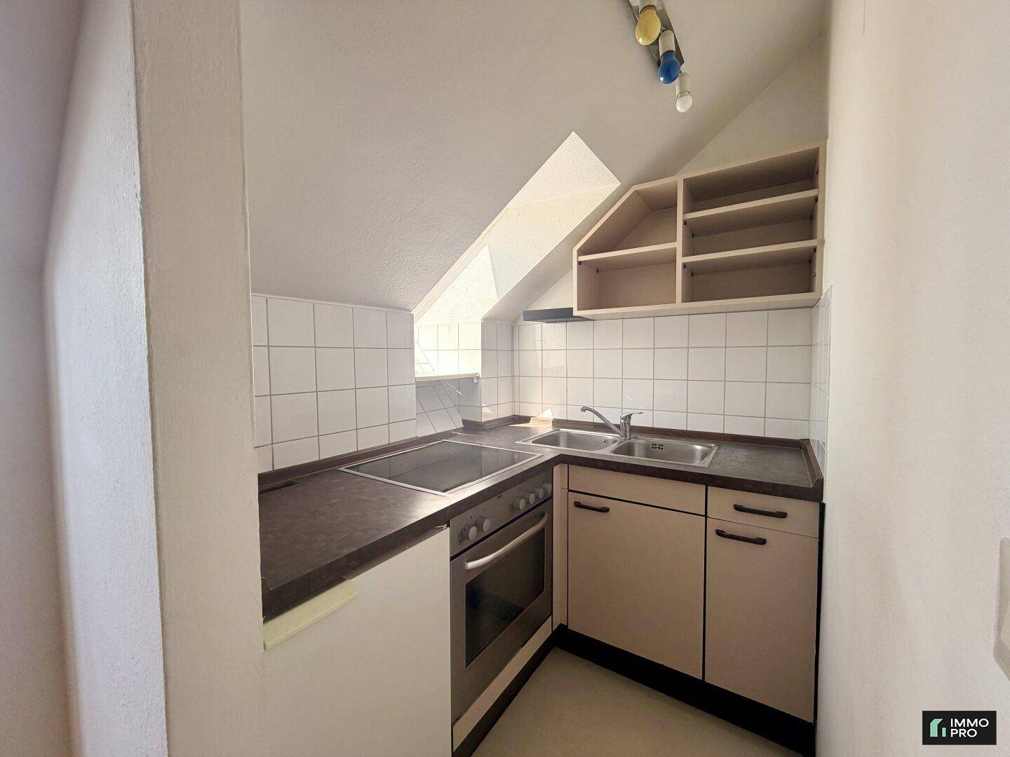 Kleine Einbauküche in Dachschräge mit Herd, Spüle und praktischen Oberschränken.