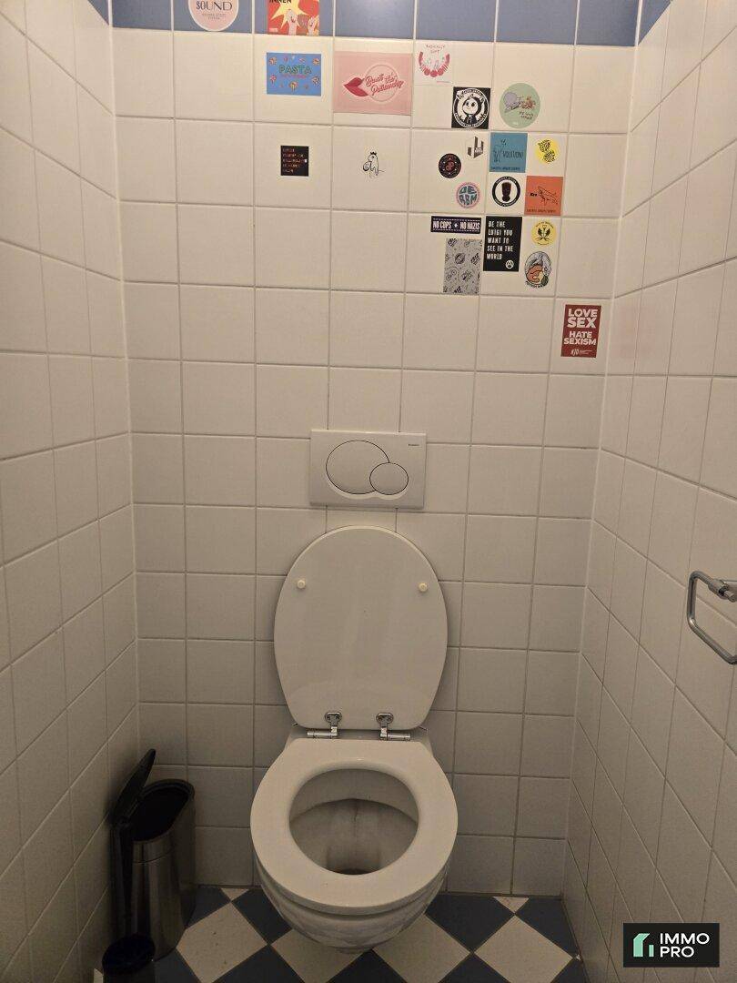 Separates WC mit Wand-WC und weißen Fliesen, dekoriert mit bunten Aufklebern.