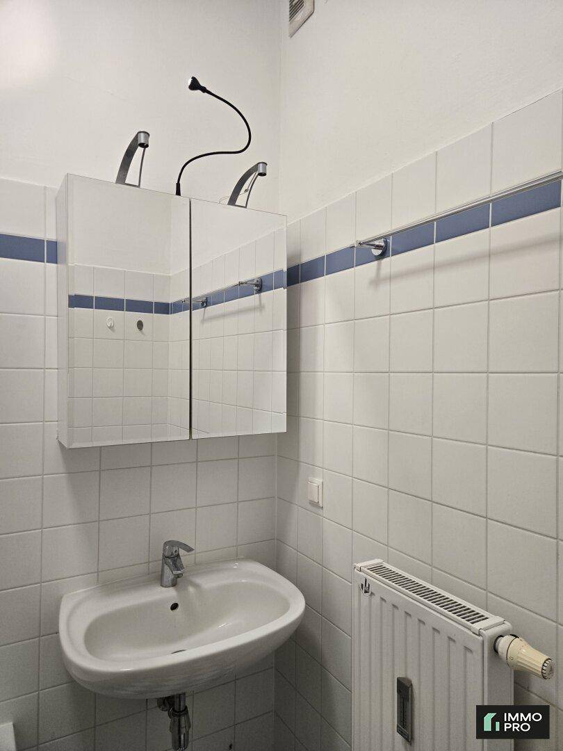 Badezimmer mit Waschbecken, Spiegelschrank und weißen Fliesen mit blauer Zierleiste.