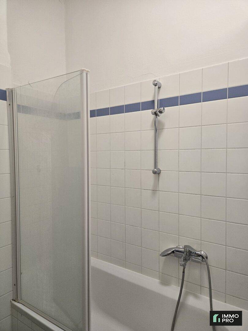 Badezimmer mit Badewanne und Duschvorrichtung, umgeben von weißen Fliesen und blauer Bordüre.