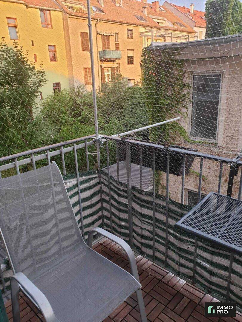 Kleiner Balkon mit Holzboden, Sitzgelegenheit und Blick auf die umliegenden Gebäude.