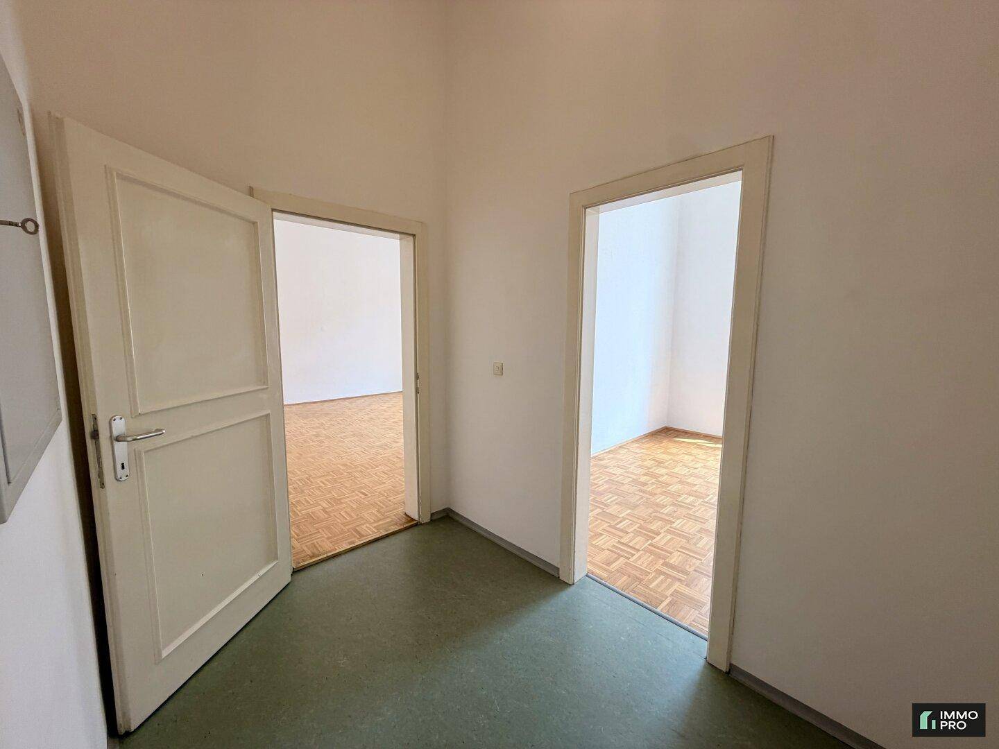 Flur mit grünem Bodenbelag, der zu zwei hellen Zimmern mit Parkettboden führt.