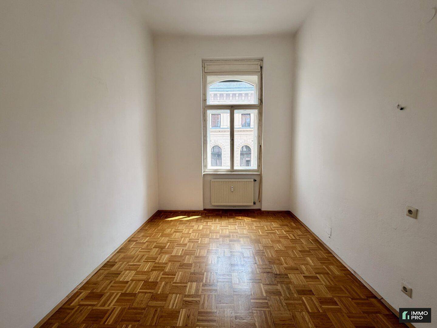 Geräumiges Zimmer mit klassischem Parkettboden und einem großen Fenster für viel Helligkeit.