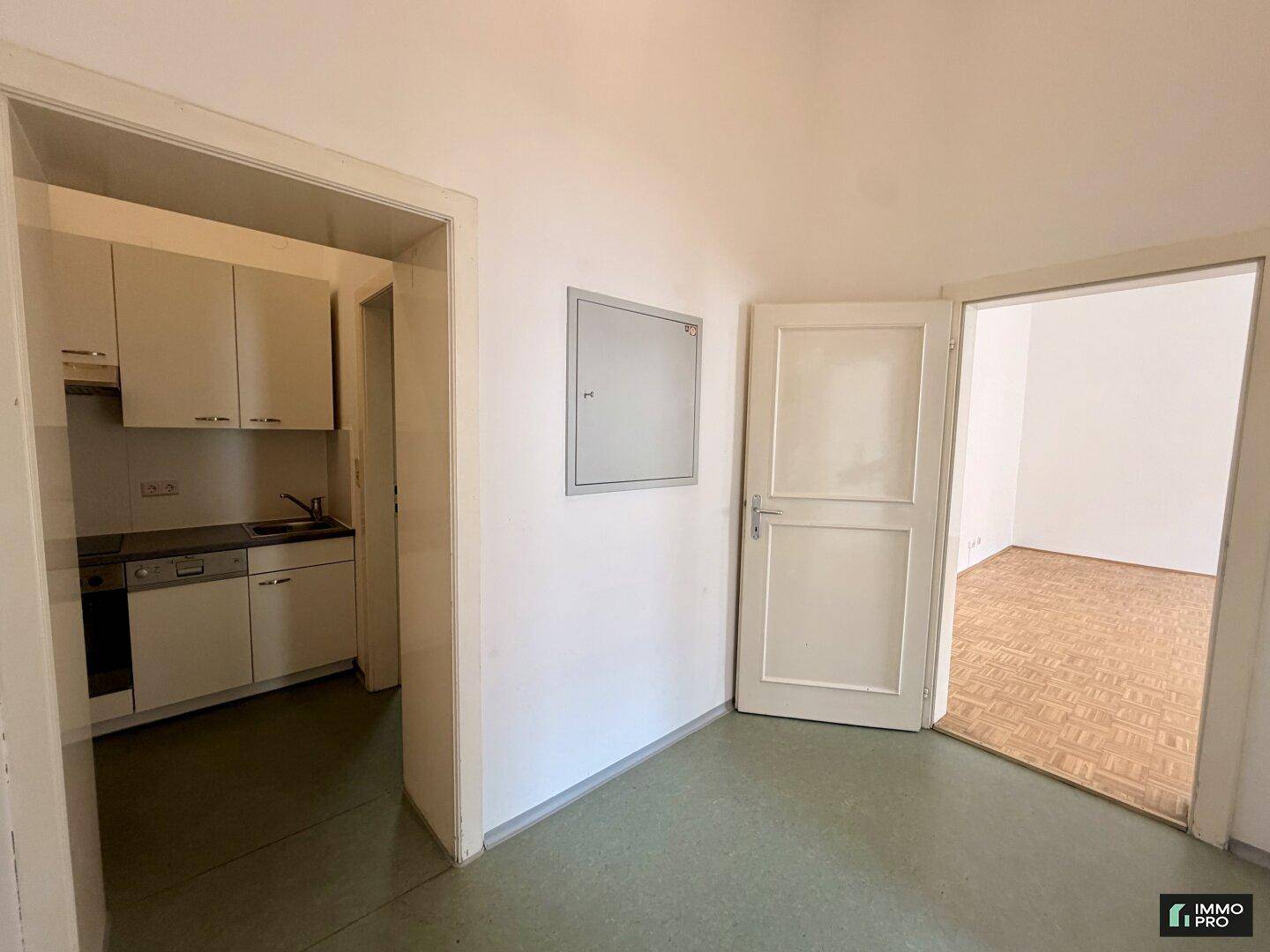Flur mit Zugang zur kompakten Küche und einem weiteren Zimmer mit Parkettboden.