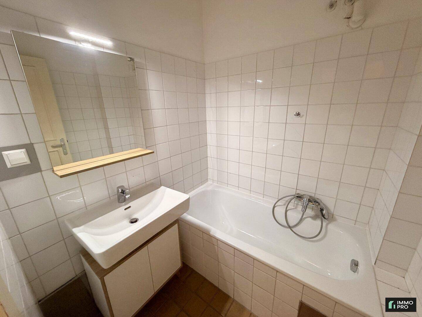 Badezimmer mit weißen Fliesen, einem Waschbeckenunterschrank und einer Badewanne.