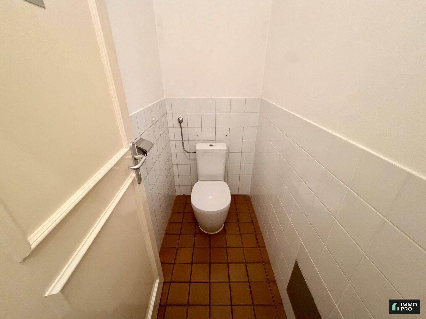 Separates WC mit weißen Wandfliesen und Terrakotta-Bodenfliesen für Gäste.