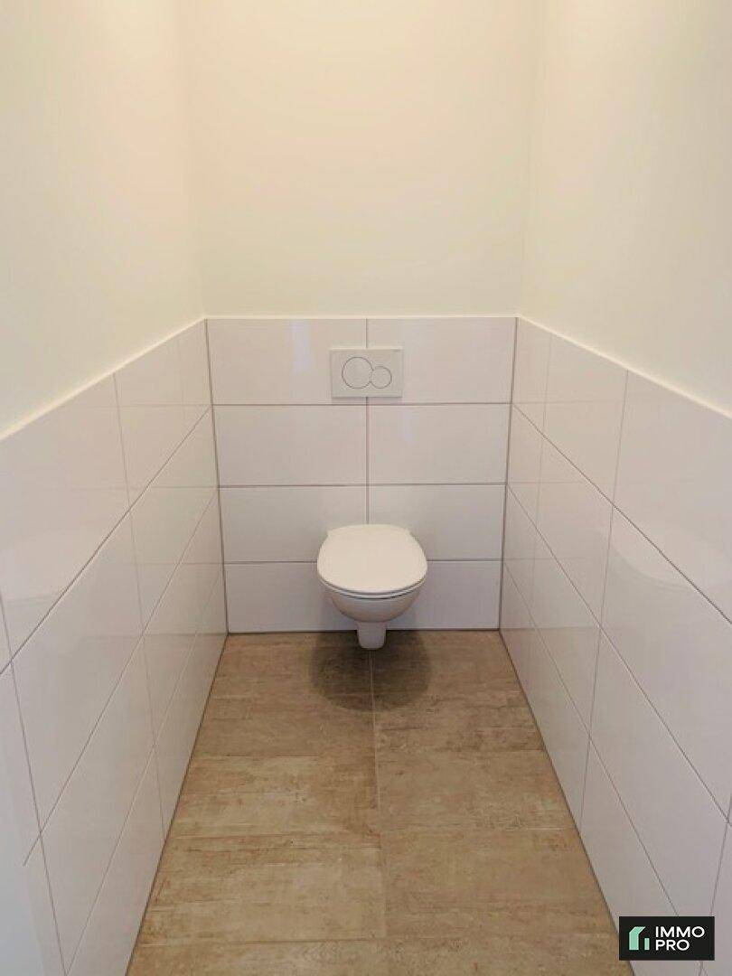 Separates WC mit wandhängender Toilette und hellen Fliesen an den Wänden.