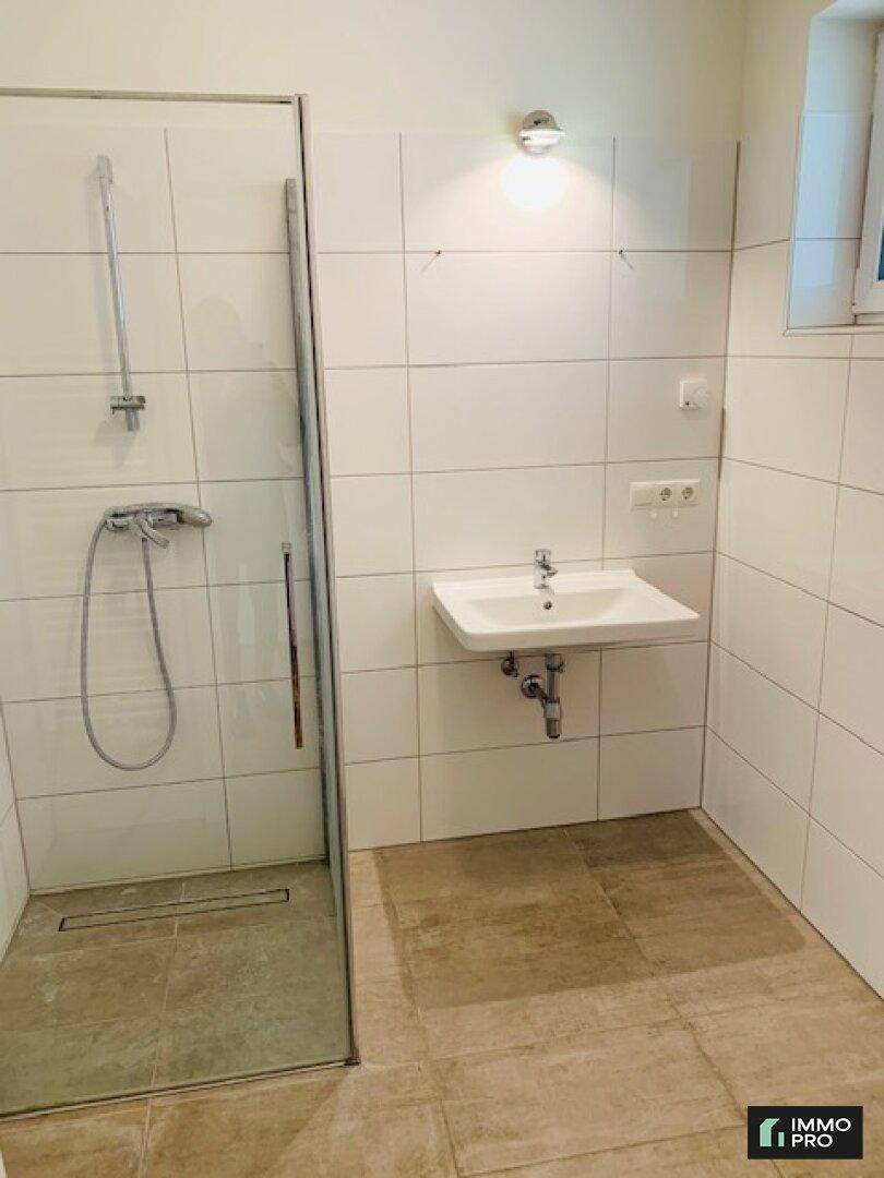 Modernes Badezimmer mit ebenerdiger Dusche, Waschbecken und Fenster für Tageslicht.