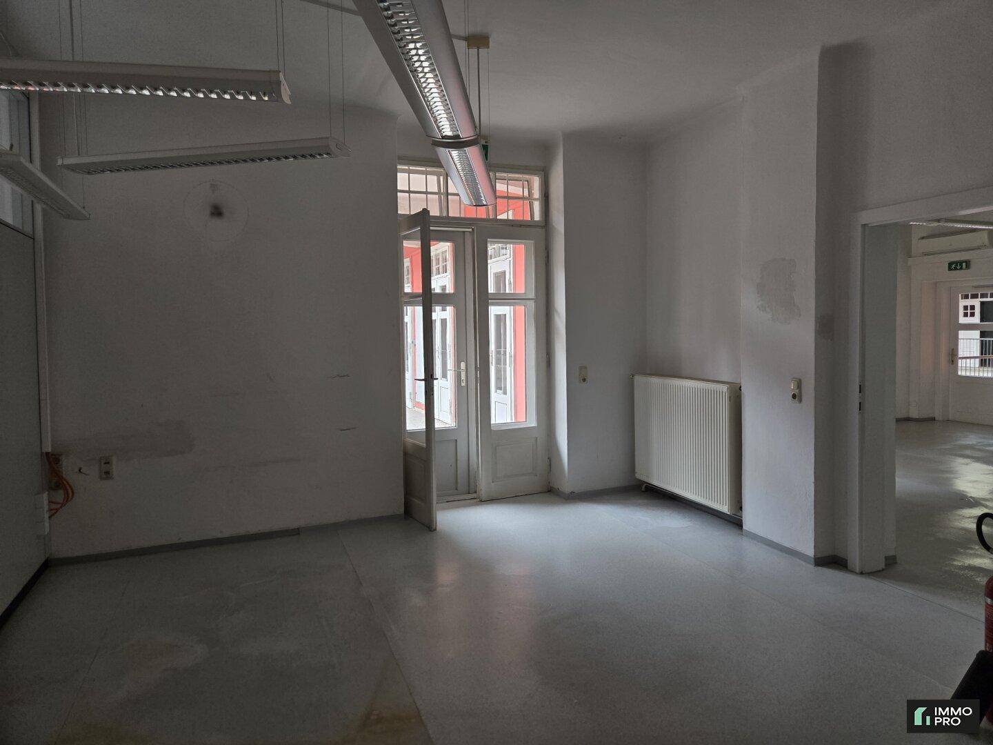 Leerer Büroraum mit großen Fenstertüren und Heizkörpern, bereit für neue Mieter.