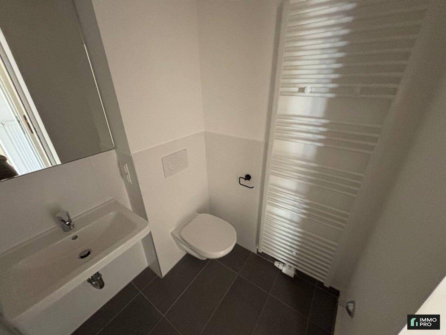 Modernes WC mit wandhängender Toilette, Waschbecken und beheiztem Handtuchhalter.
