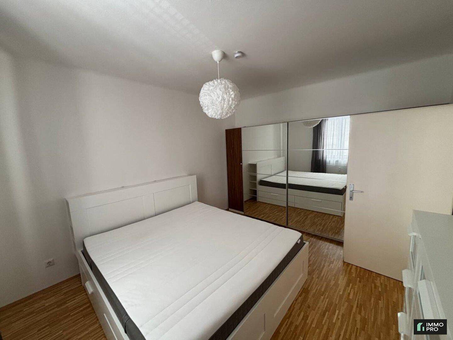 Schlafzimmer mit Doppelbett, Spiegelschrank und hellem Parkettboden.
