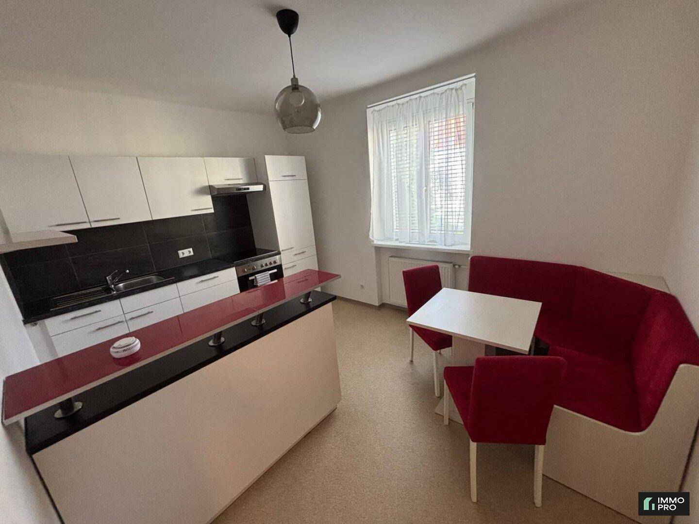 Moderne Küche mit weißen Schränken, roter Frühstücksbar und Essbereich.