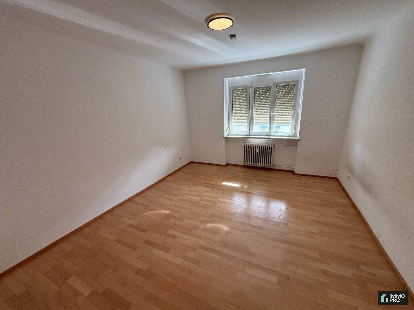 Geräumiges Zimmer mit Holzfußboden, einem Fenster mit Rollläden und einem Deckenlicht.