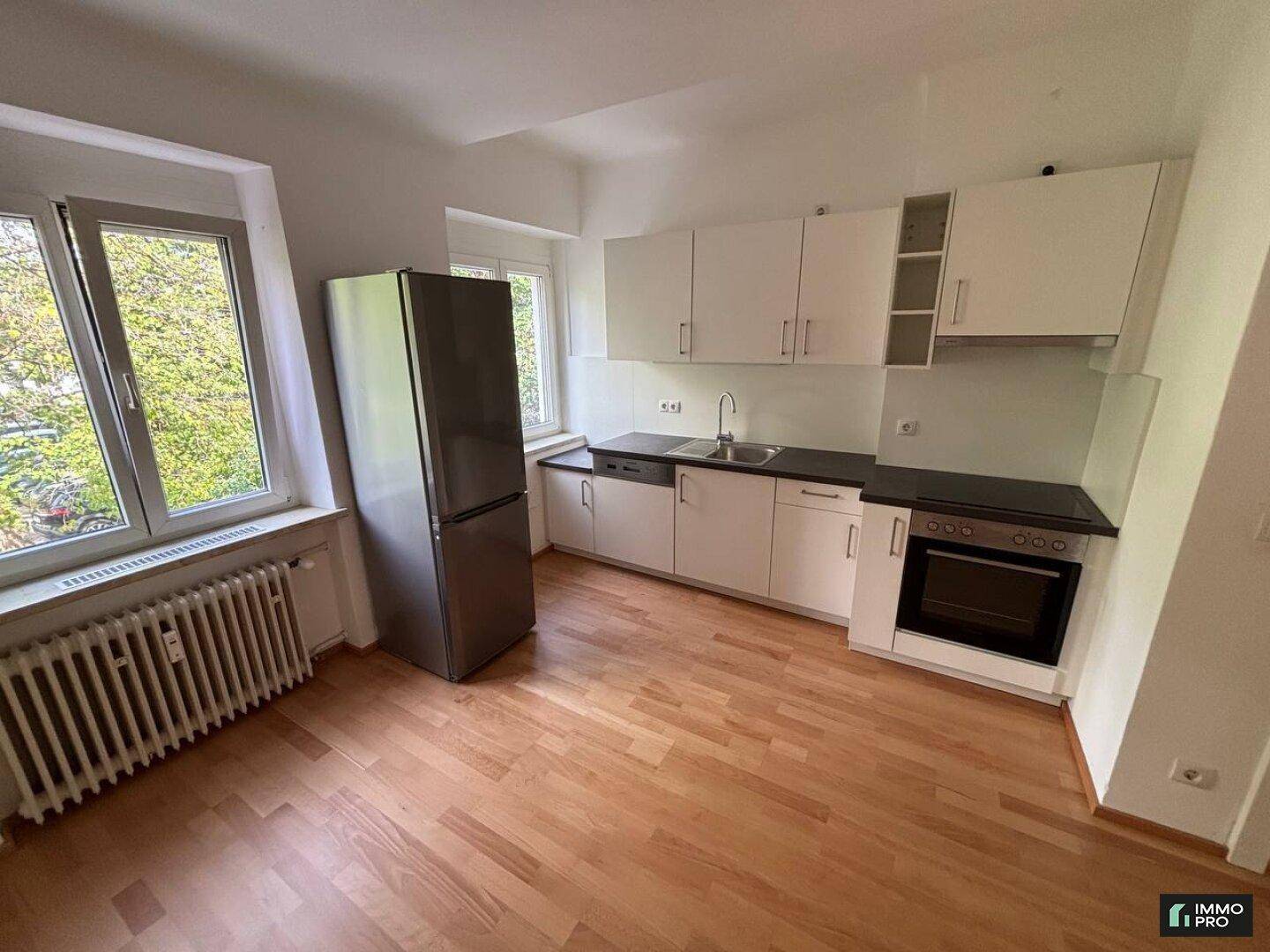 Helle Einbauküche mit weißen Fronten, dunkler Arbeitsplatte und großem Kühlschrank.