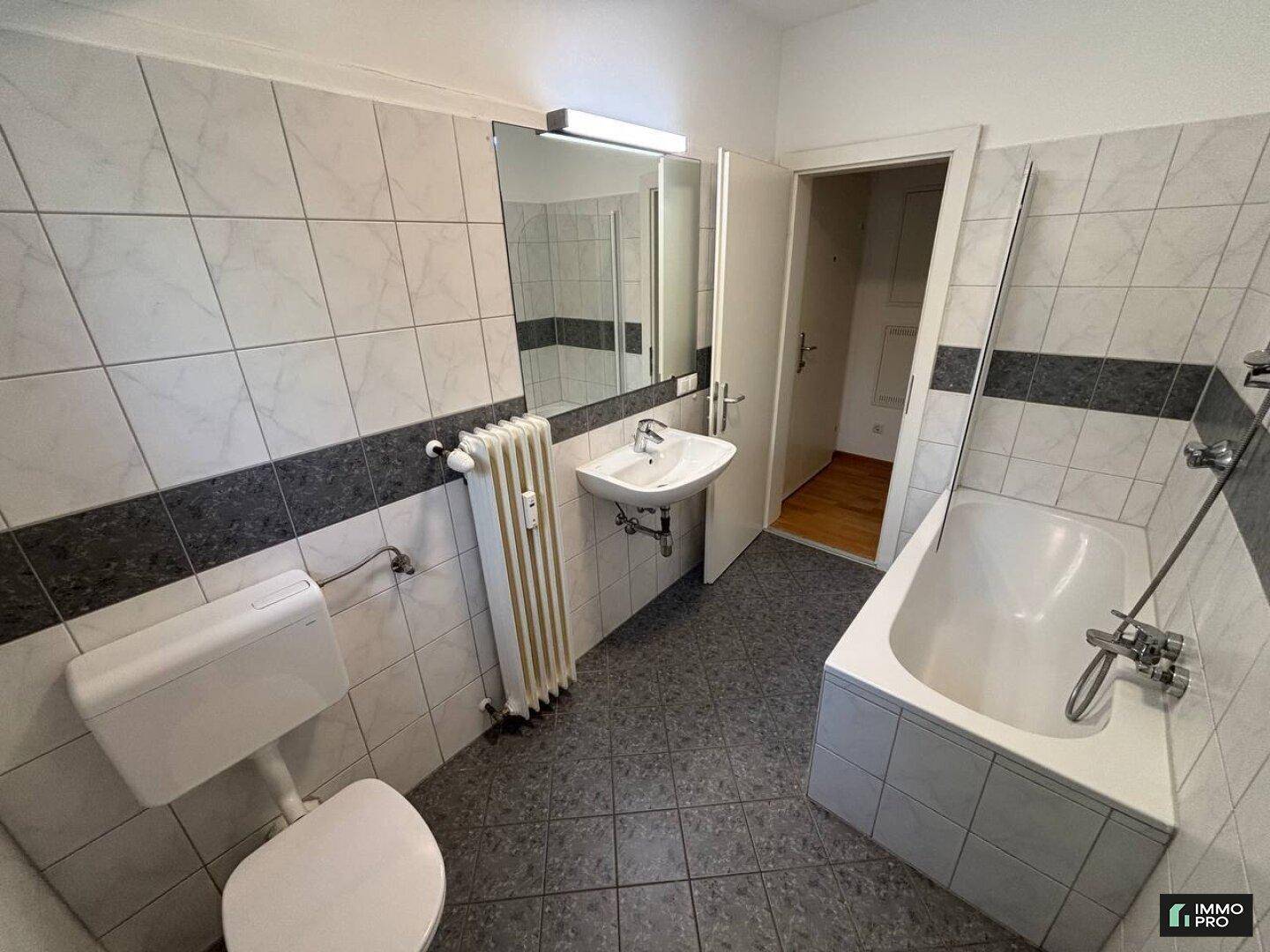Badezimmer mit Badewanne, WC, Waschbecken und weiß-grauen Fliesen an Wänden und Boden.