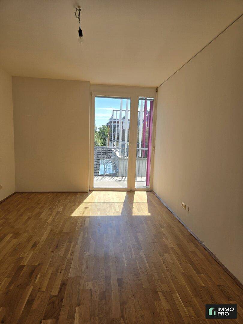 Heller Raum mit Parkettboden und Zugang zu einem Balkon, durchflutet von Sonnenlicht.