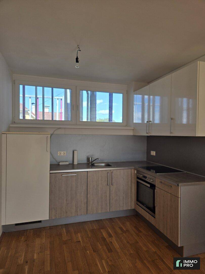 Funktionale Küche mit hellen Holzschränken, weißen Oberschränken und Fenster.