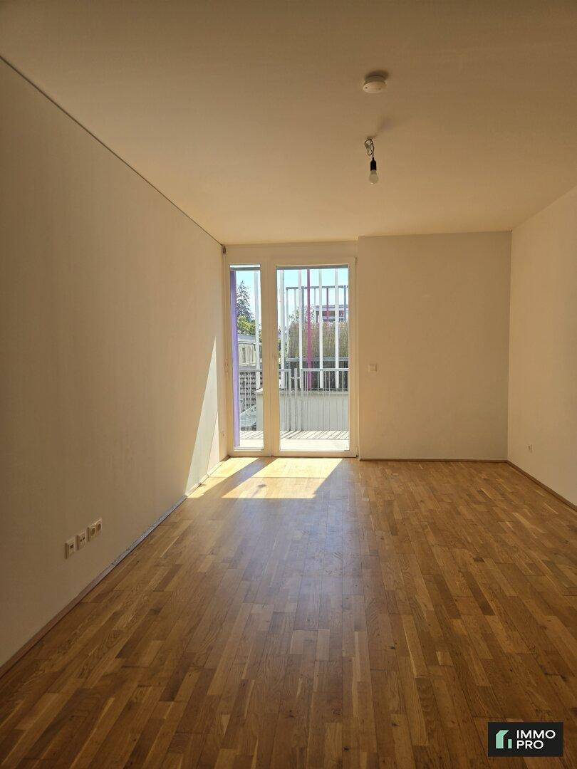 Lichtdurchfluteter Raum mit Holzboden und Balkontür, ideal für Wohn- oder Schlafbereich.