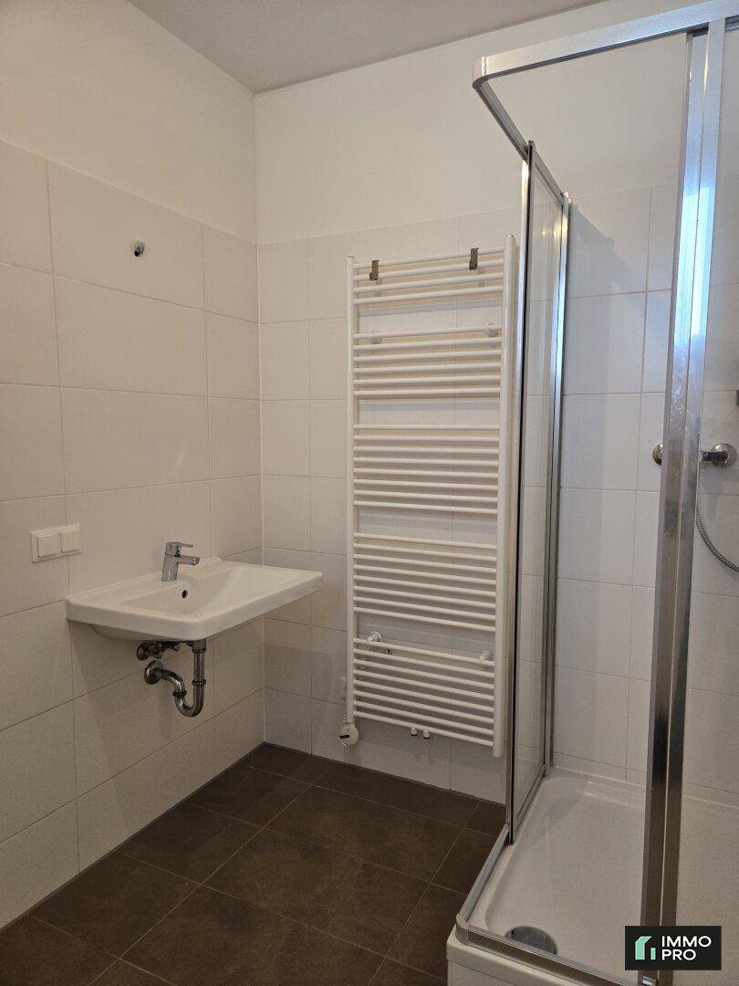 Helles Badezimmer mit weißen Fliesen, Dusche und beheiztem Handtuchhalter.
