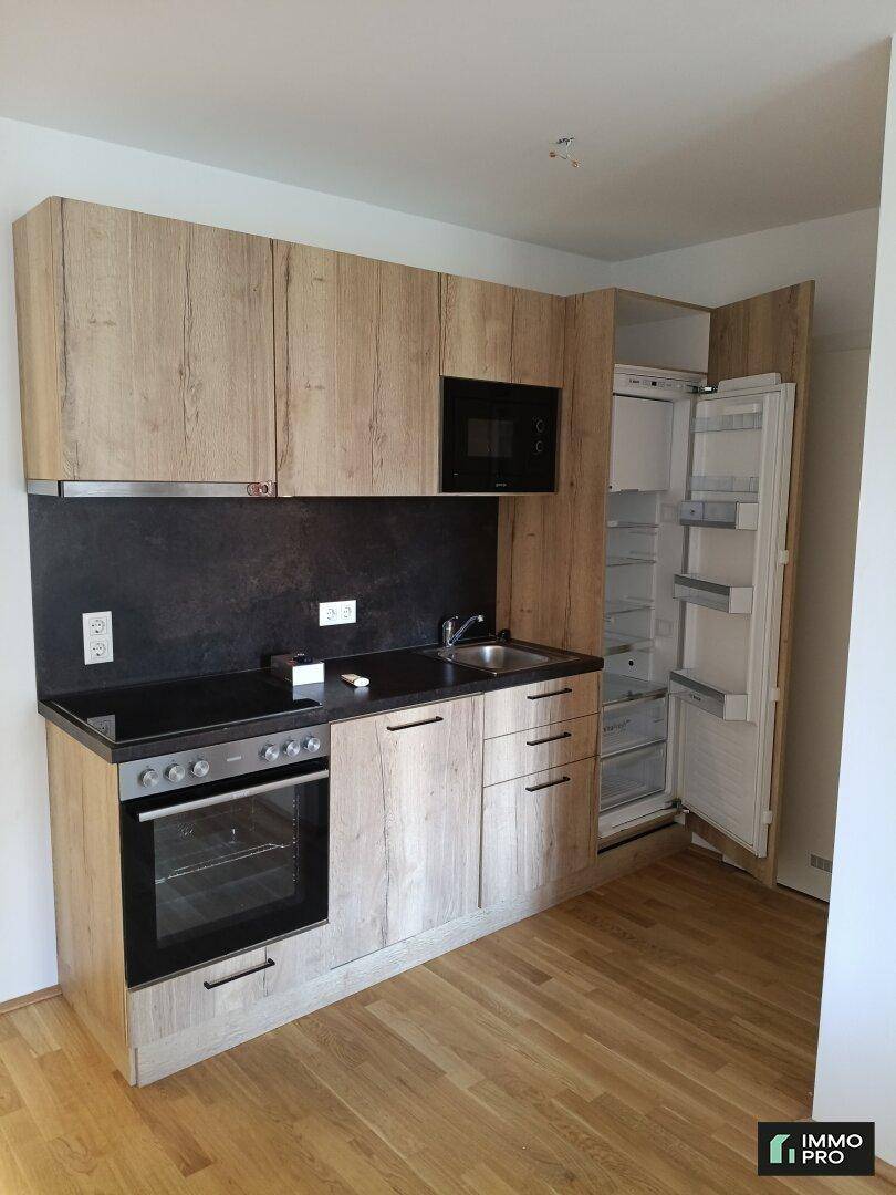 Moderne Küchenzeile mit Holzoptik-Fronten, integrierten Geräten und dunkler Arbeitsplatte.