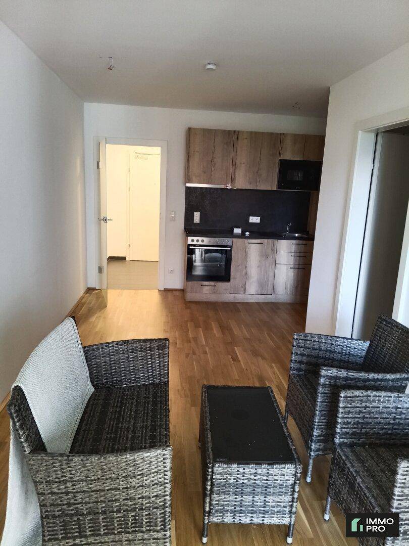 Offener Wohnbereich mit Rattanmöbeln und integrierter Küchenzeile, ideal für kompaktes Wohnen.