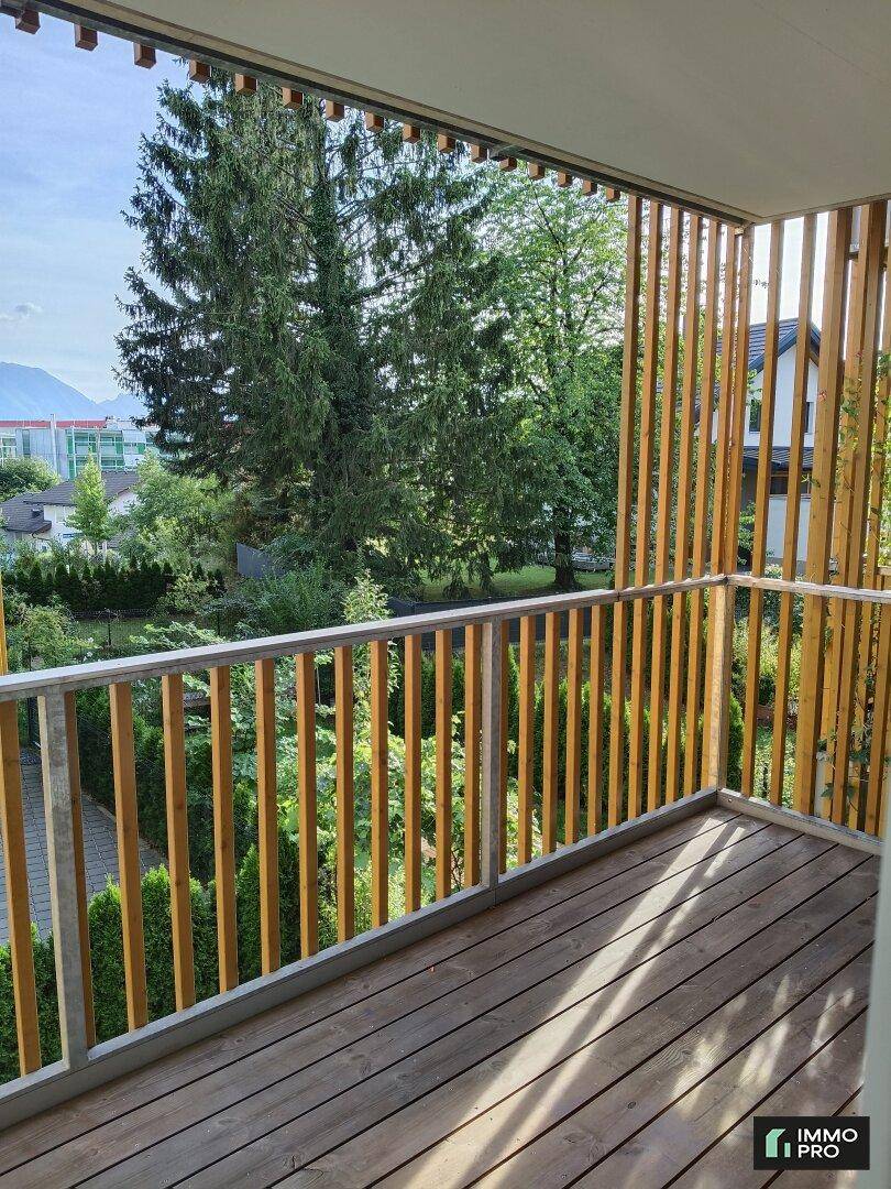 Geräumiger Balkon mit Holzboden und grüner Aussicht, umgeben von Bäumen und Natur.