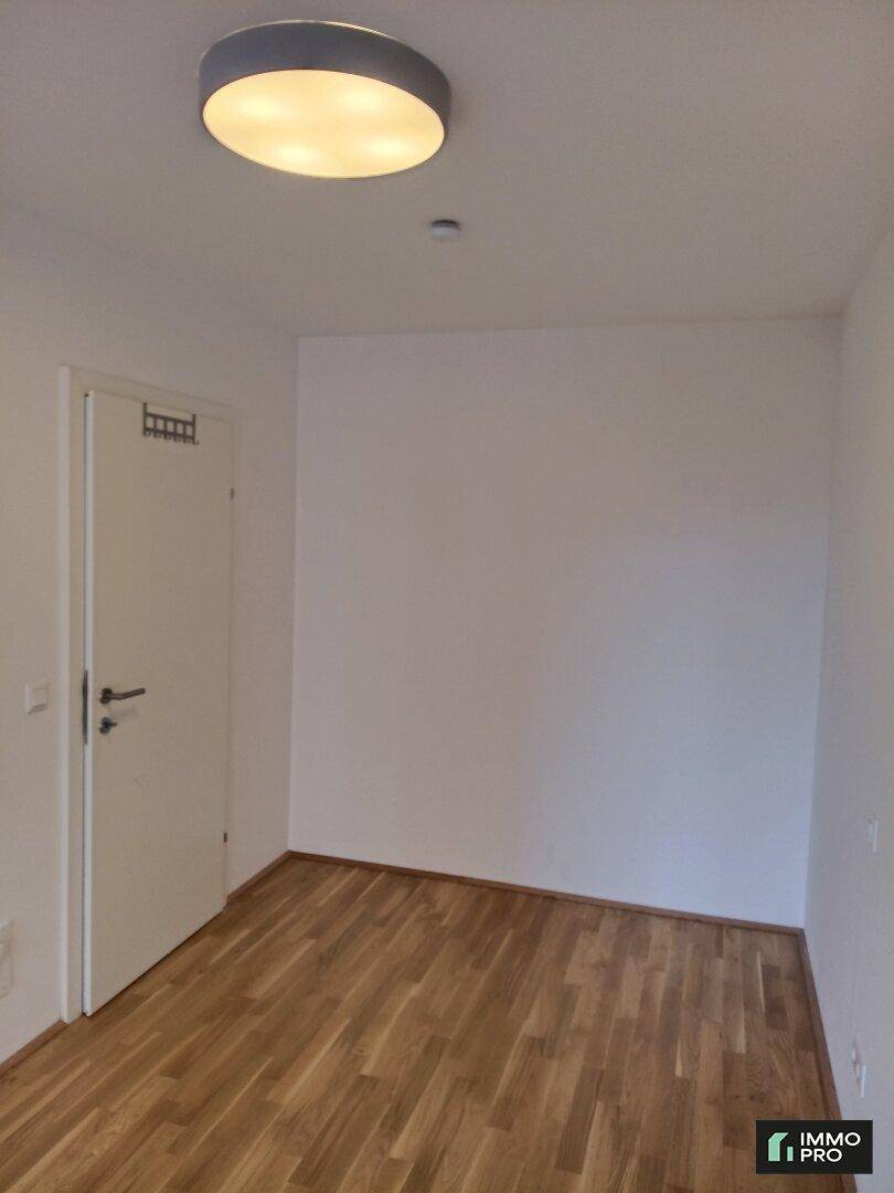Schlichtes Zimmer mit Holzboden und weiß gestrichenen Wänden, bereit zur individuellen Gestaltung.