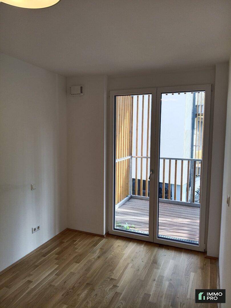Helles Zimmer mit Holzboden und Balkonzugang, bietet viel Tageslicht und frische Luft.