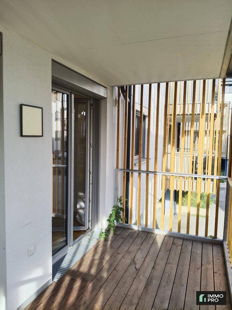Heller Balkon mit Holzboden und seitlichem Blick auf die moderne Gebäudefassade.
