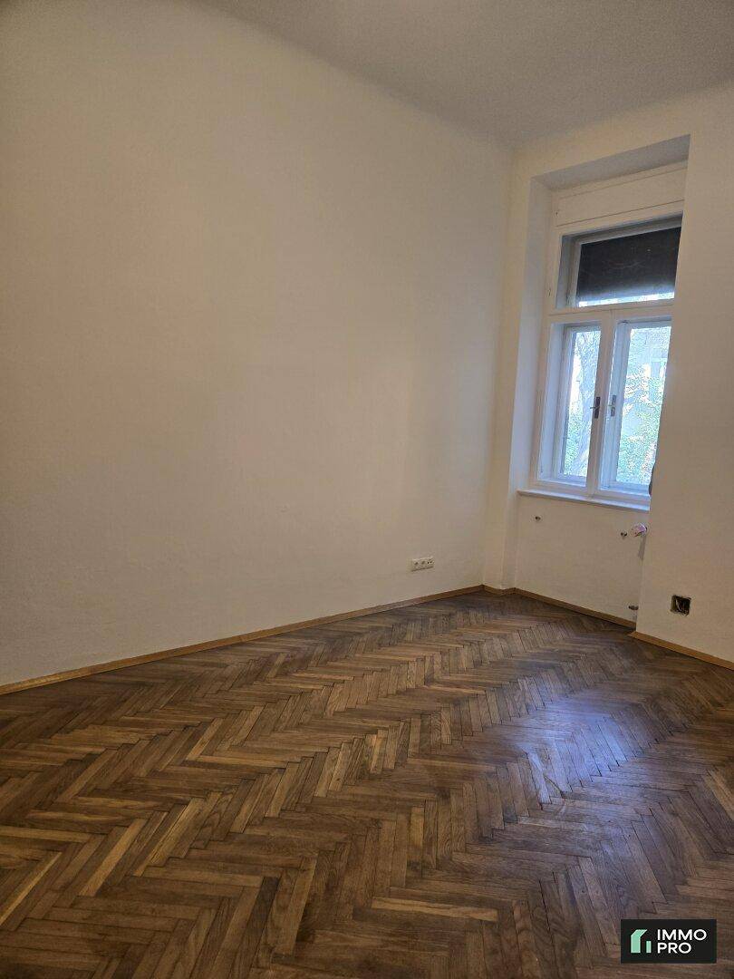 Helles Zimmer mit klassischem Fischgrätparkett und einem großen Fenster, das für eine angenehme Atmosphäre sorgt.