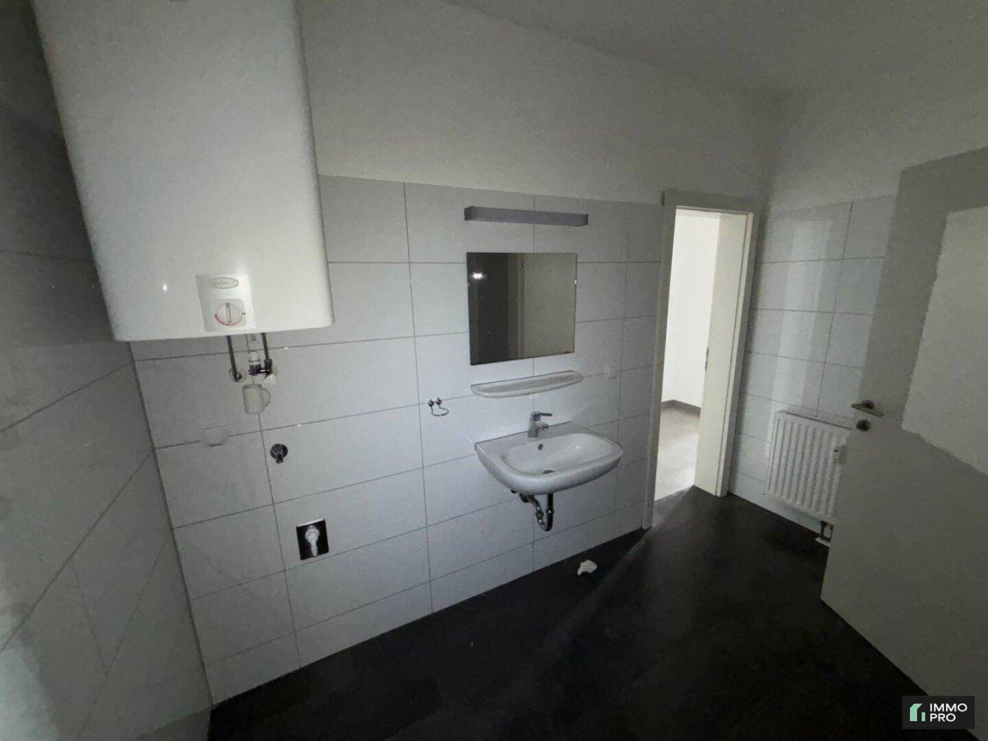 Funktionales Badezimmer mit Waschbecken, Spiegel und Wandfliesen, ausgestattet mit einem Warmwasserboiler.