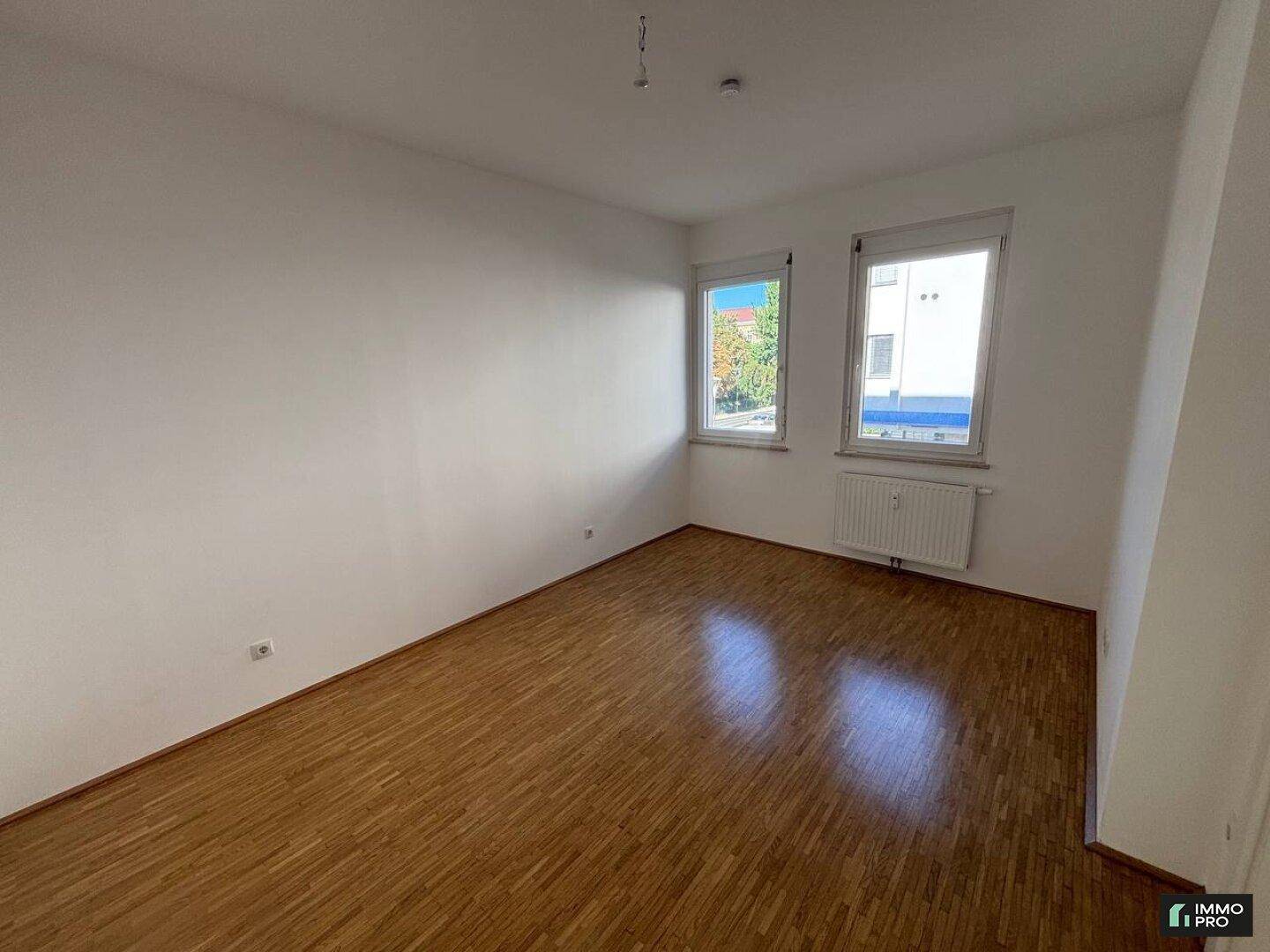Heller, unmöblierter Raum mit Parkettboden und zwei Fenstern, ideal als Wohn- oder Schlafzimmer.