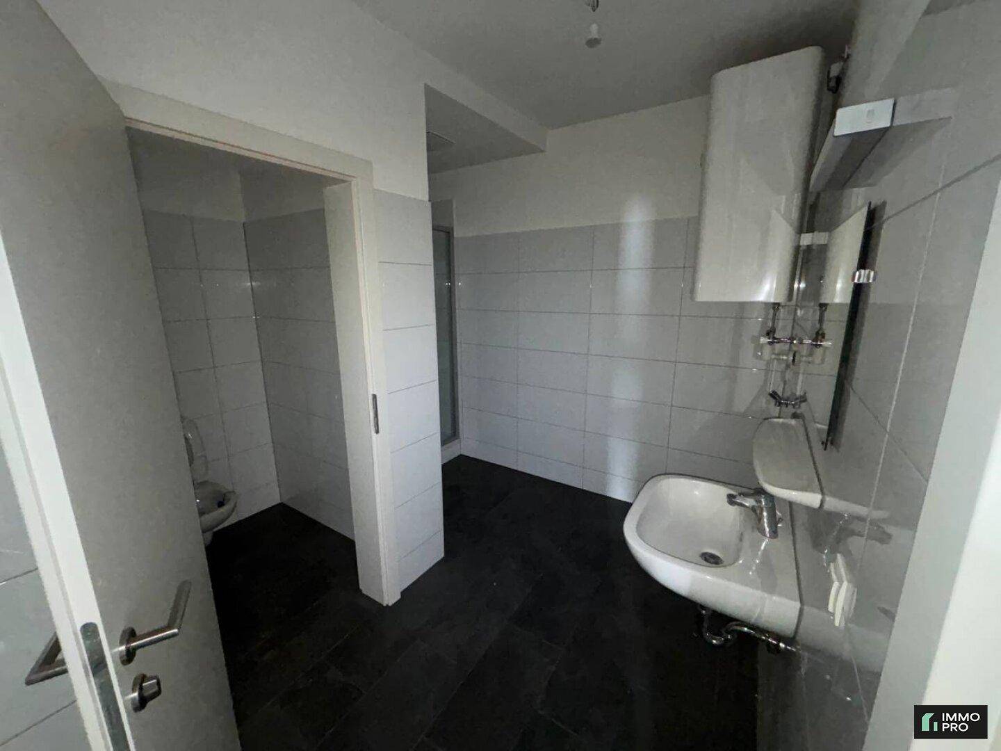 Gefliestes Badezimmer mit Waschbecken, Duschkabine und separatem WC-Bereich, in modernem Design.