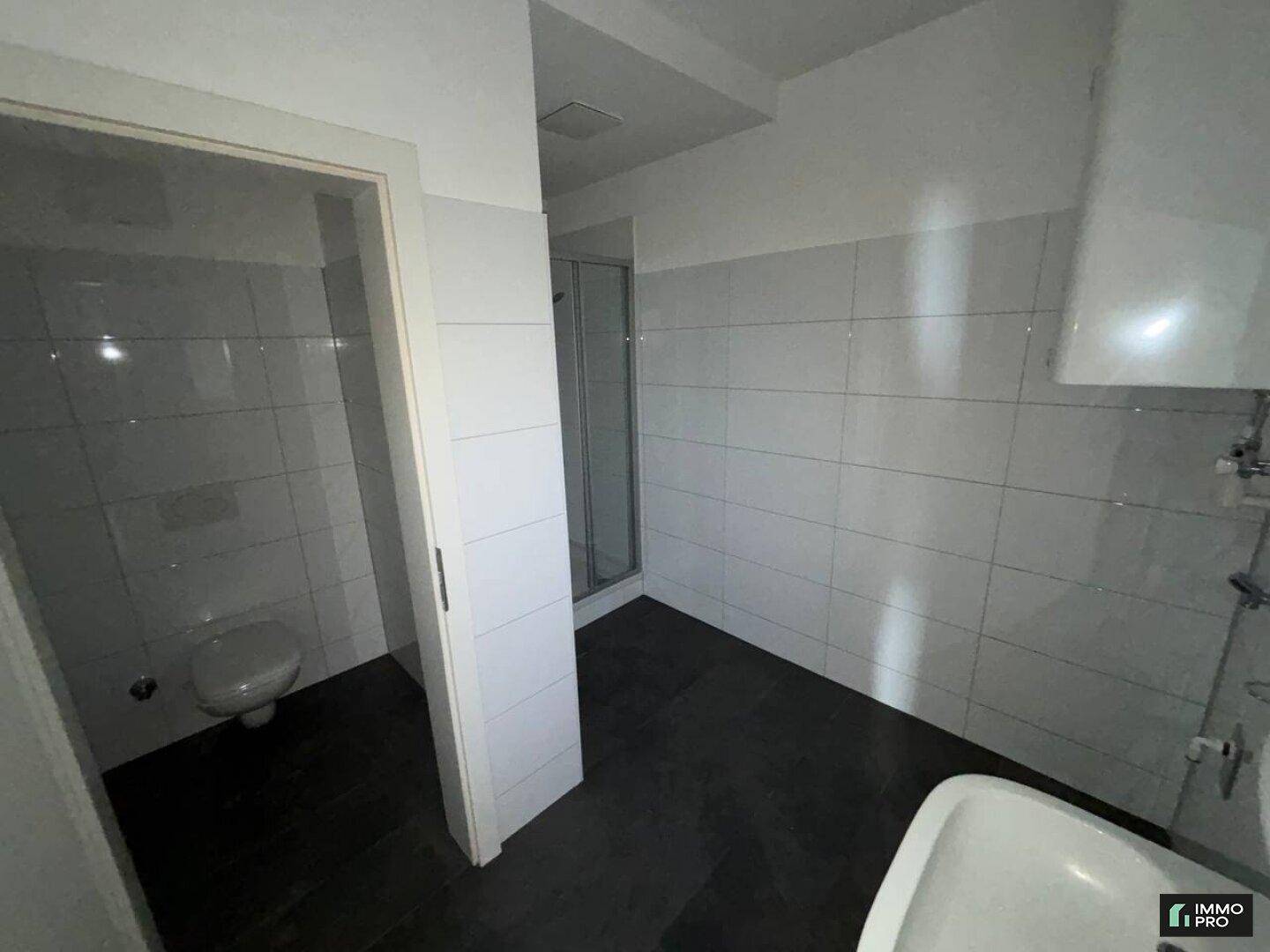 Modern gefliestes Badezimmer mit Duschkabine und wandhängendem WC, bietet eine praktische Raumaufteilung.