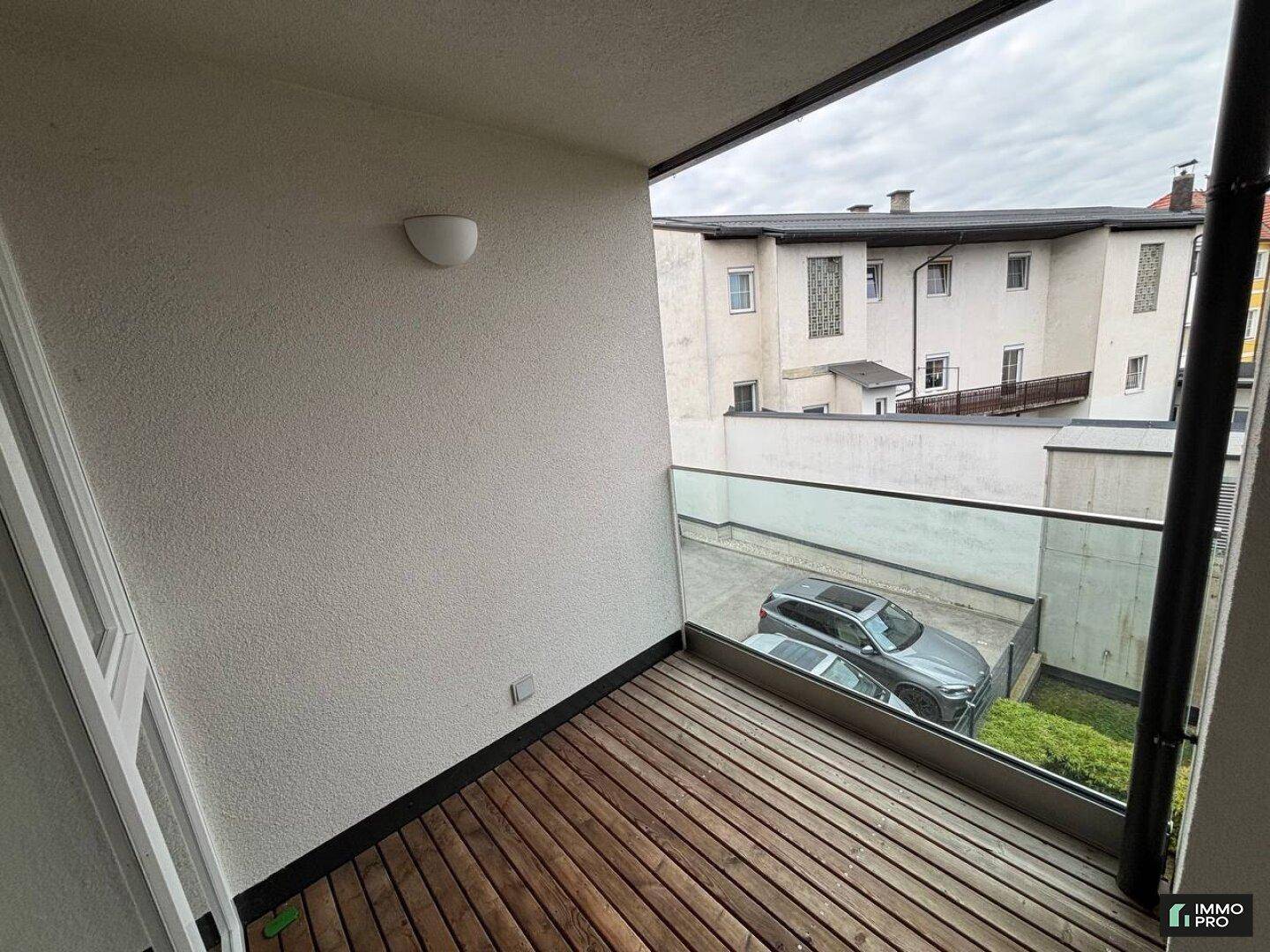 Balkon mit Holzrostboden und Glasbrüstung, bietet Blick auf den Innenhof.