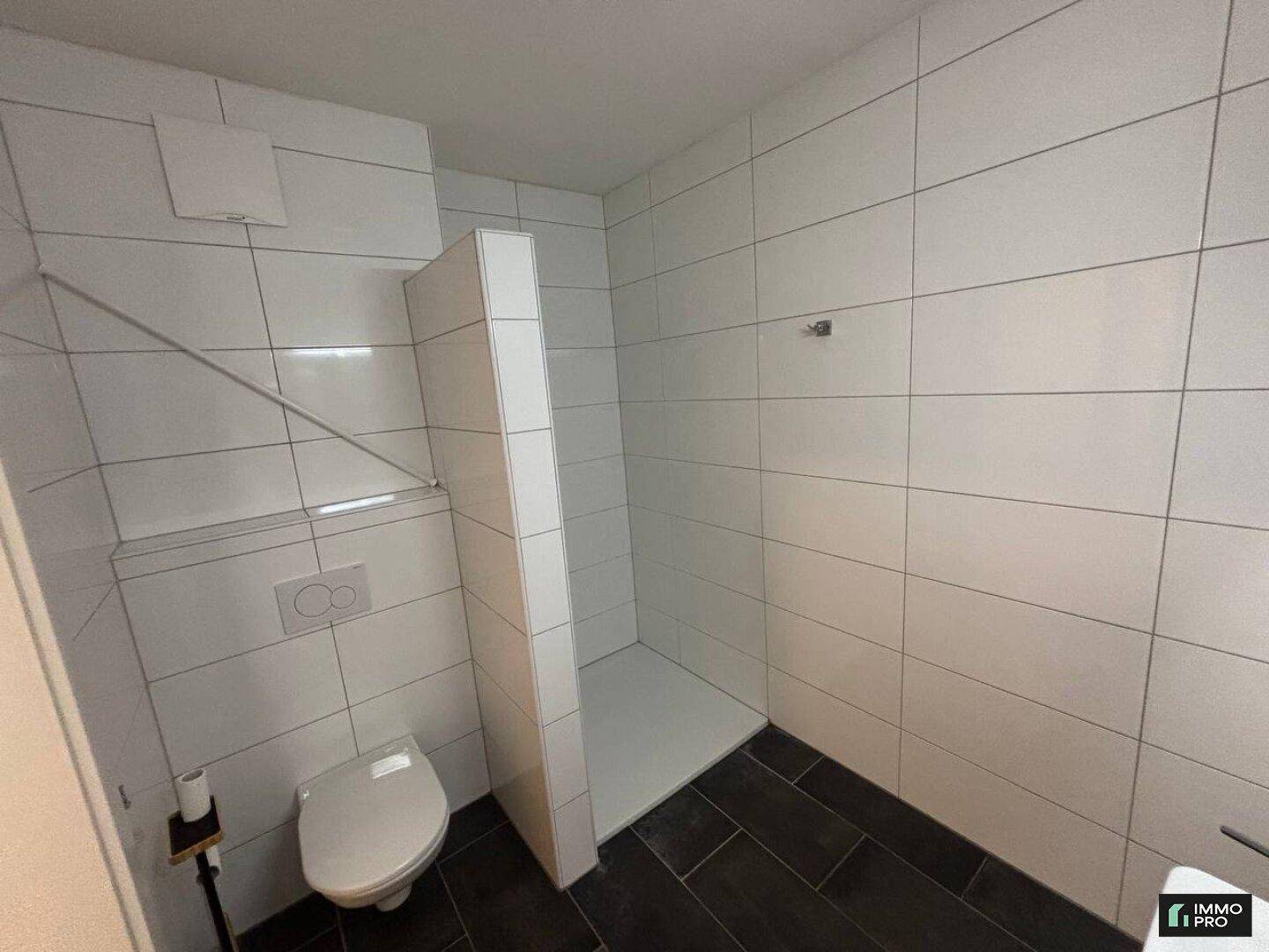 Badezimmer mit wandhängender Toilette und einer begehbaren Dusche.