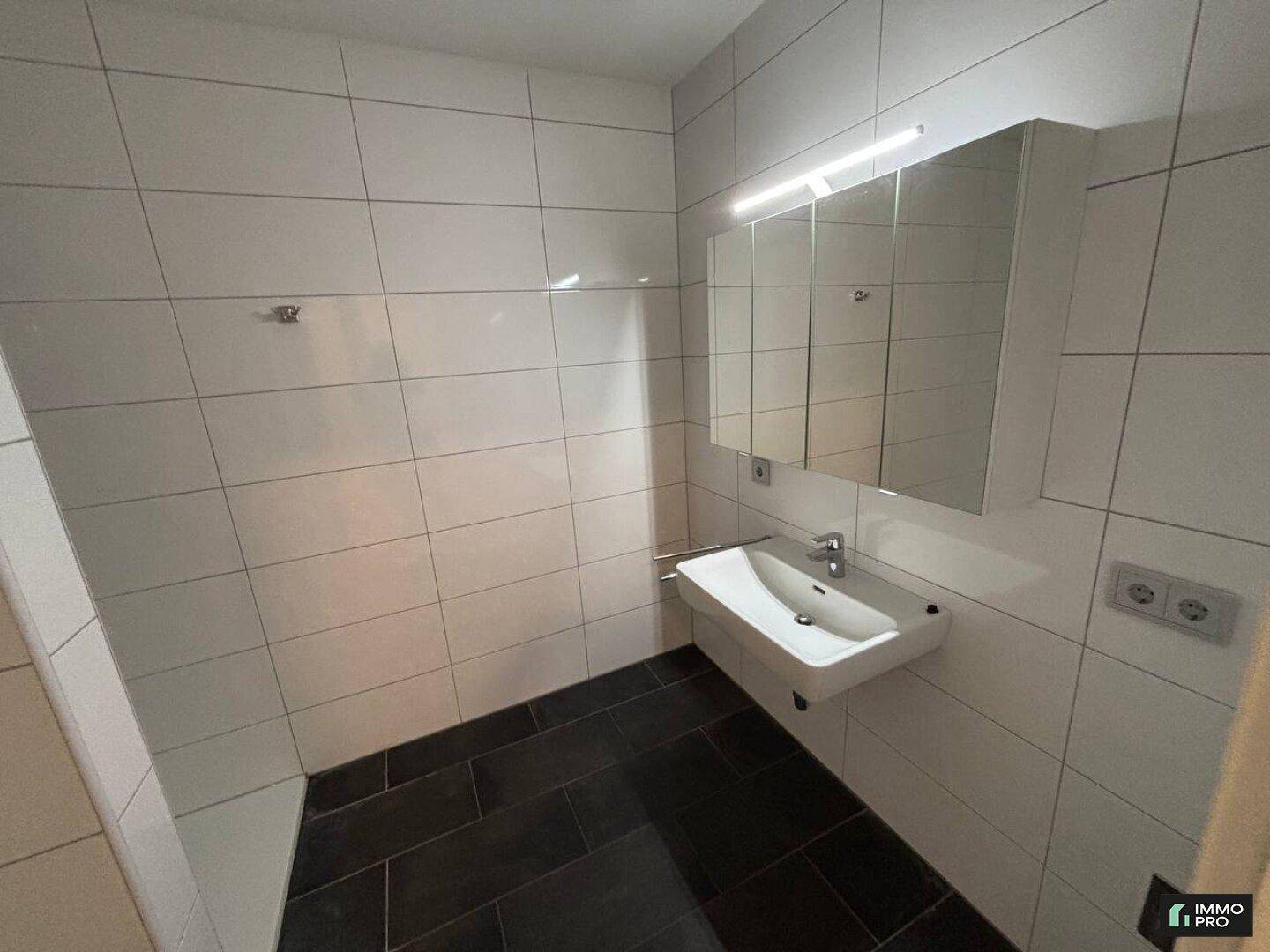 Modernes Badezimmer mit weißen Wandfliesen, dunklem Boden und Spiegelschrank.