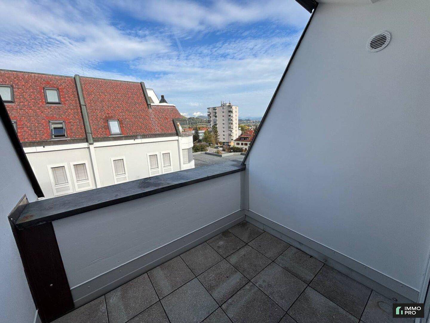Kleiner Balkon mit Fliesenboden und Blick auf die umliegenden Gebäude und den Himmel.