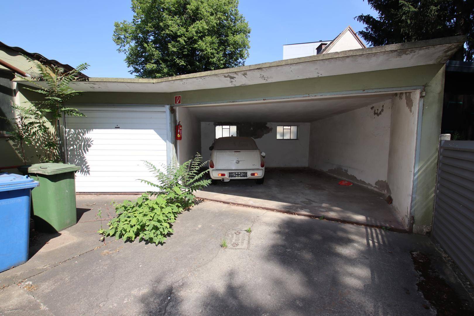 Offene Garage und Carport mit einem geparkten Auto und einem geschlossenen Garagentor auf der linken Seite.