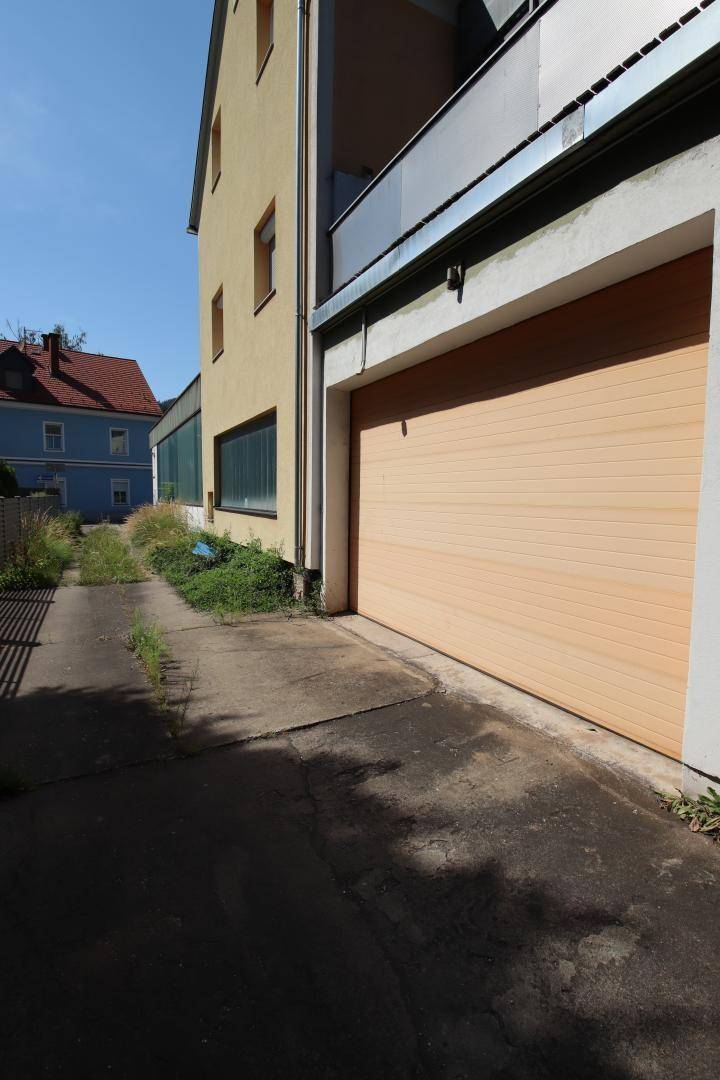 Seitenansicht des Gebäudes mit einer Zufahrt und einem Garagentor aus Holz in hellem Farbton.