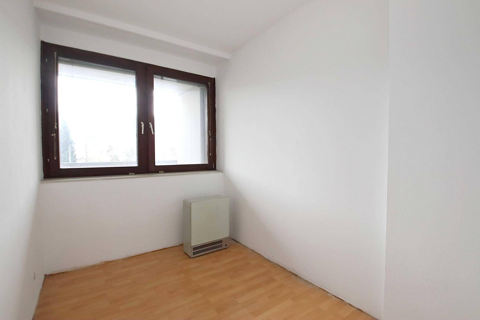 Heller, leerer Raum mit Laminatboden und großem Fenster.