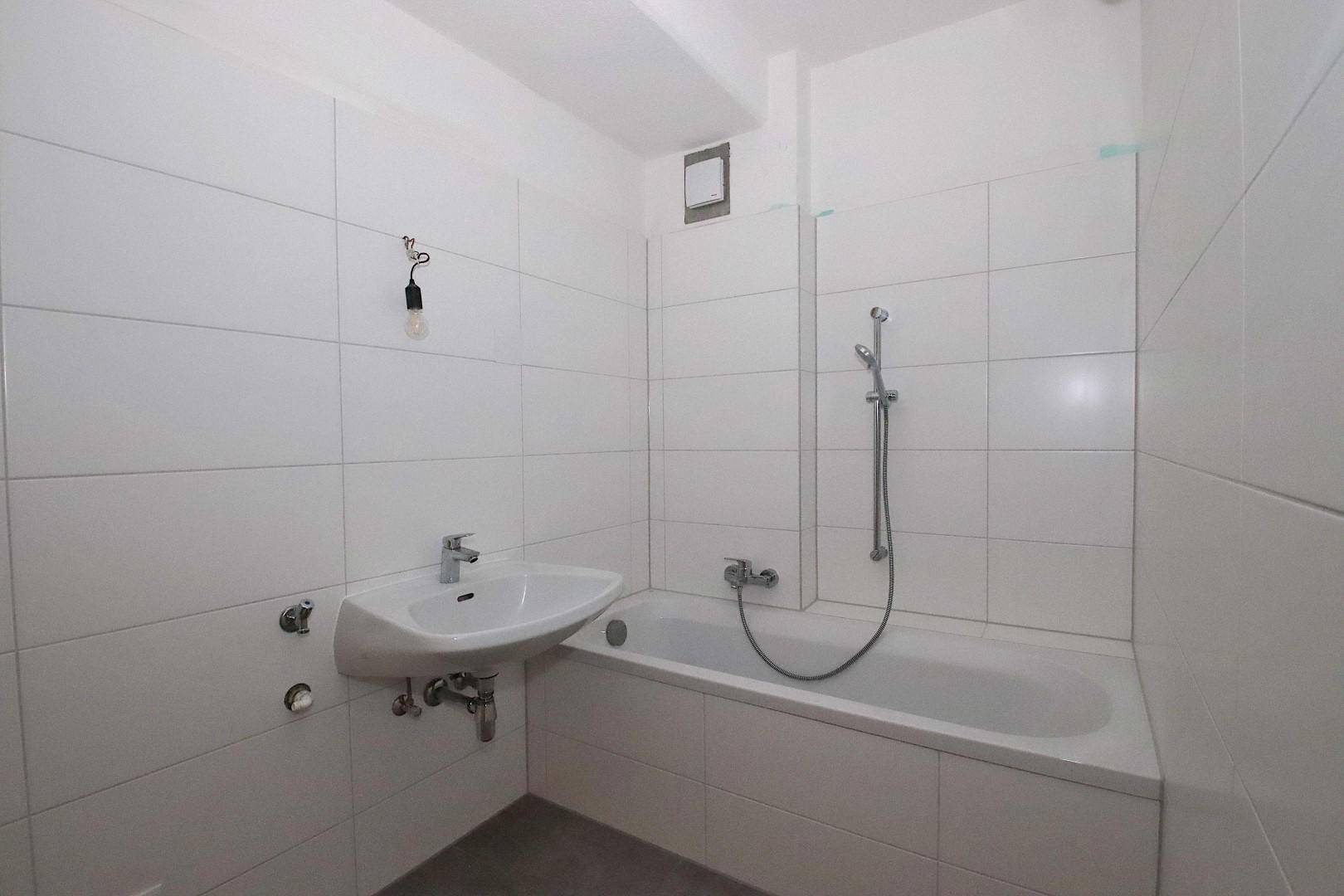 Funktionales Badezimmer mit Badewanne, Waschbecken und weißen Fliesen.