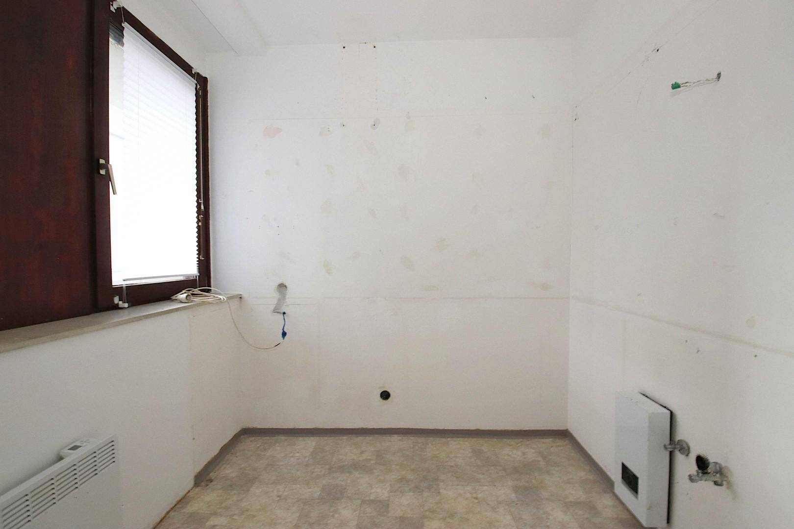 Leerer Raum mit Fenster, Heizkörper und sichtbaren Wasseranschlüssen.