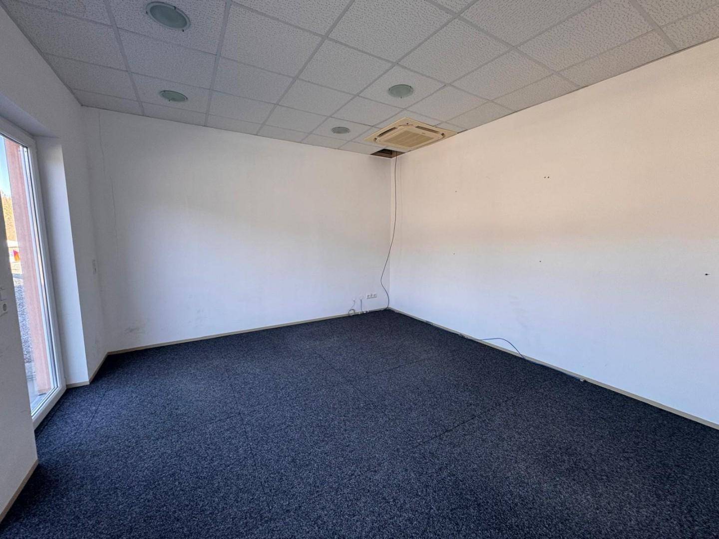 Heller Büroraum mit Teppichboden, abgehängter Decke und einer sichtbaren Klimaanlage.