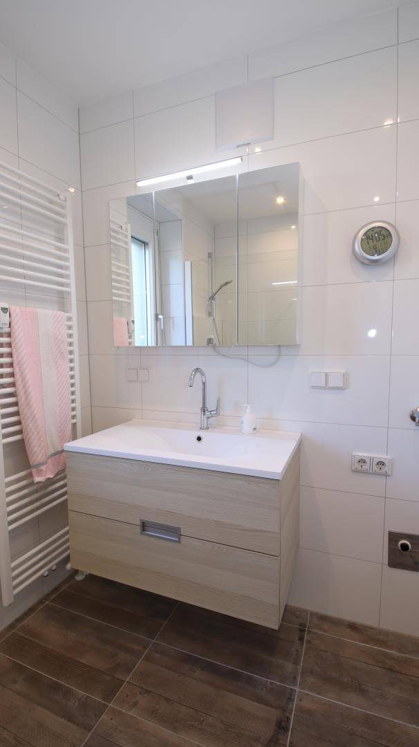 Modernes Badezimmer mit Waschtisch, Spiegelschrank, Handtuchheizkörper und Fliesenboden.