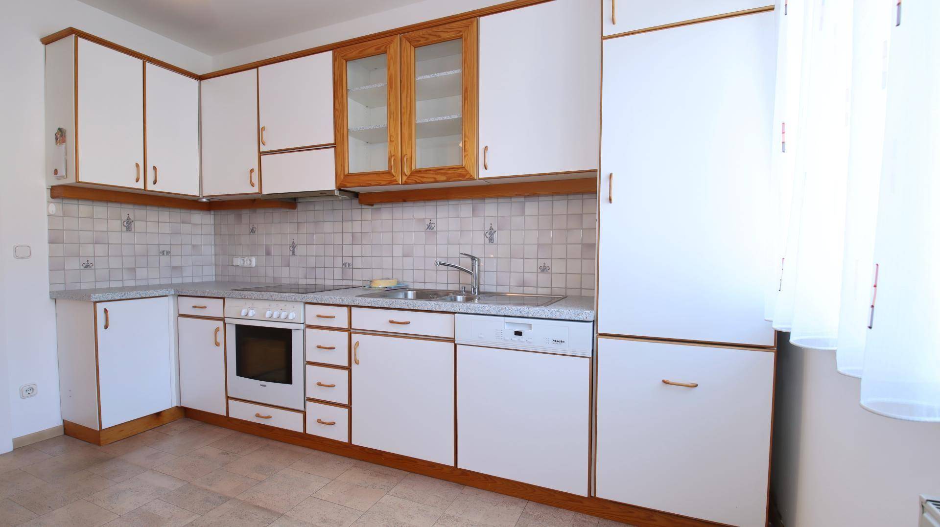 Eckküche mit weißen Fronten, Holzrahmen, integrierten Geräten und heller Fliesenrückwand.