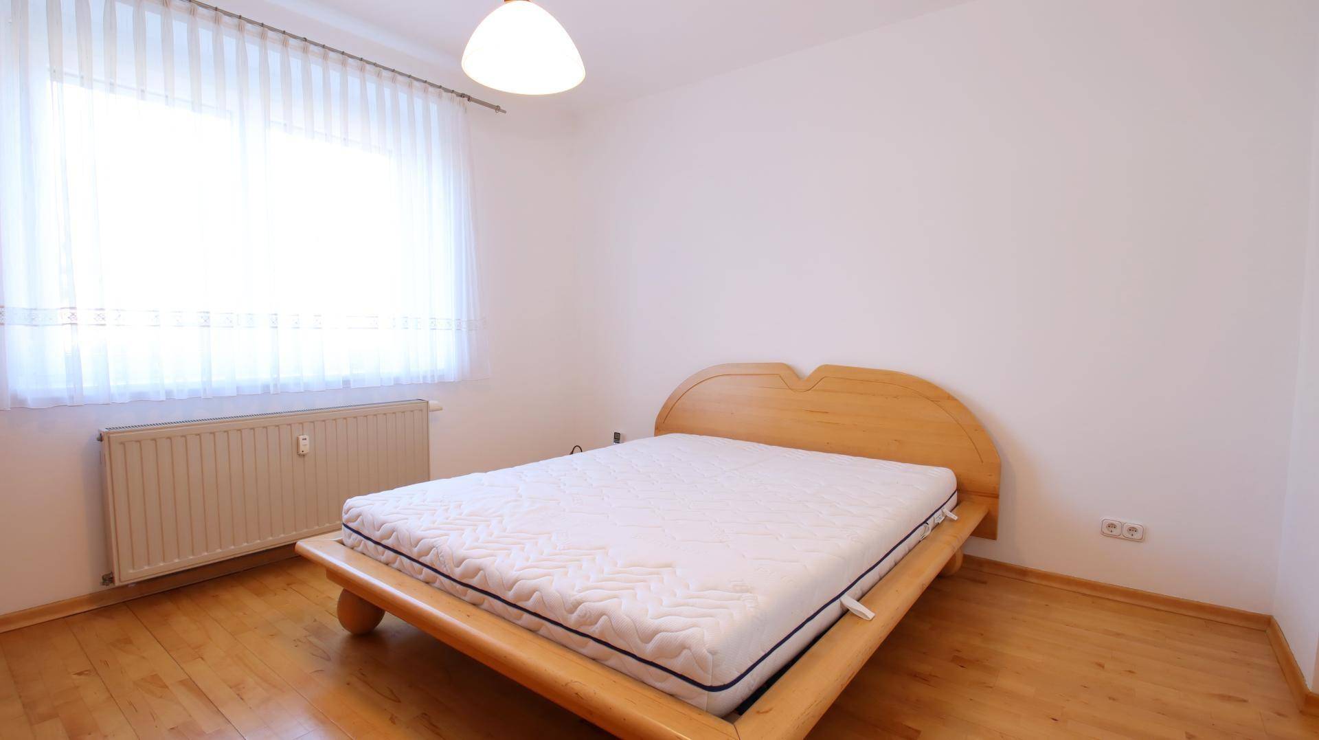 Helles Schlafzimmer mit Holzbett, Parkettboden und großem Fenster für viel Tageslicht.